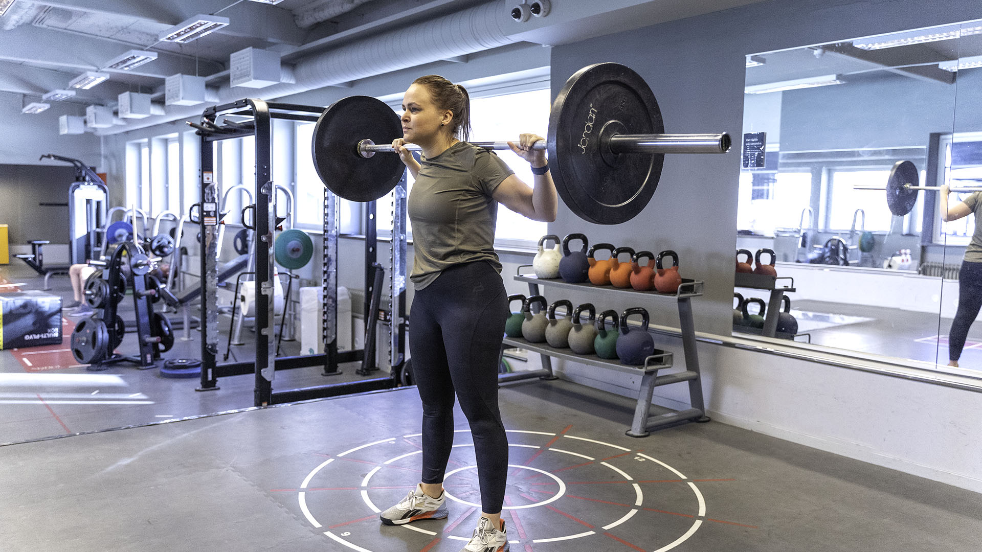 Kvinna utför knäböj med skivstång, med rak rygg och fötterna höftbrett isär