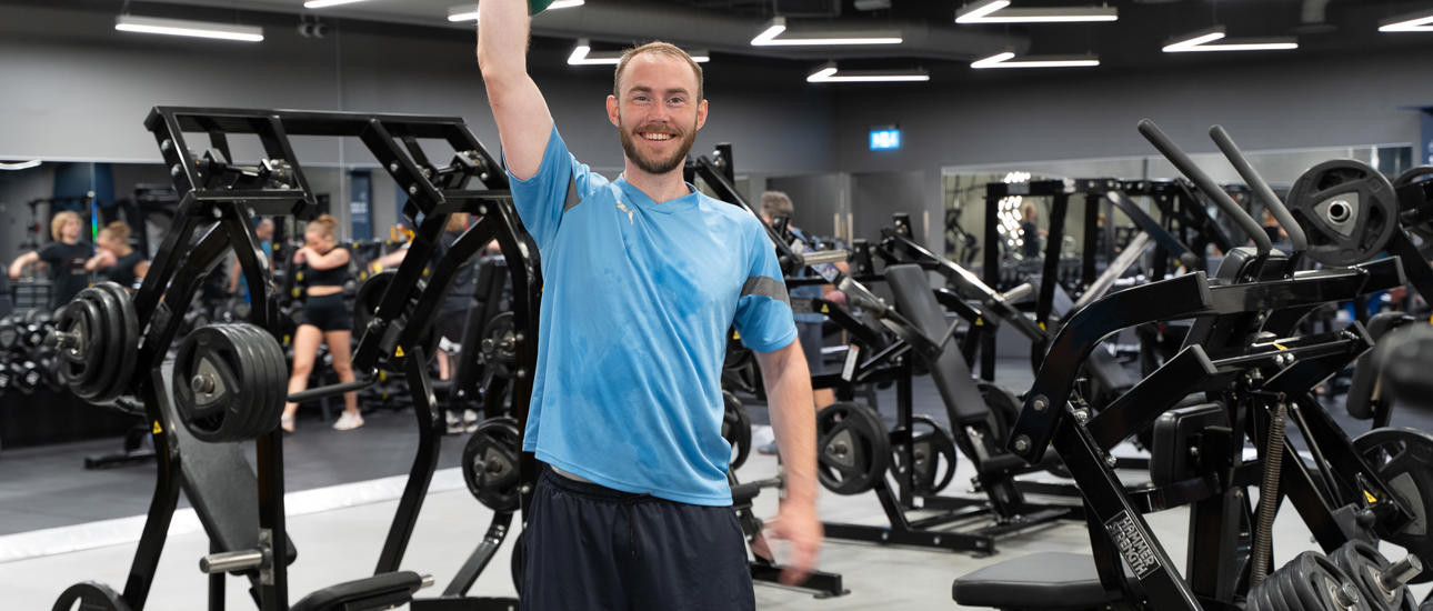 Glad mann på treningssenter trener og holder opp en kettlebell