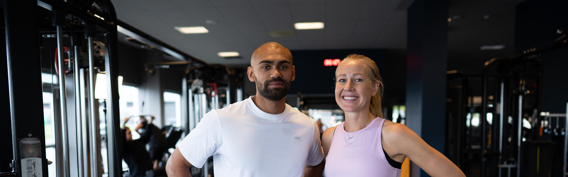 En manliga och kvinnlig medlem ler och tittar in i kamera på gym