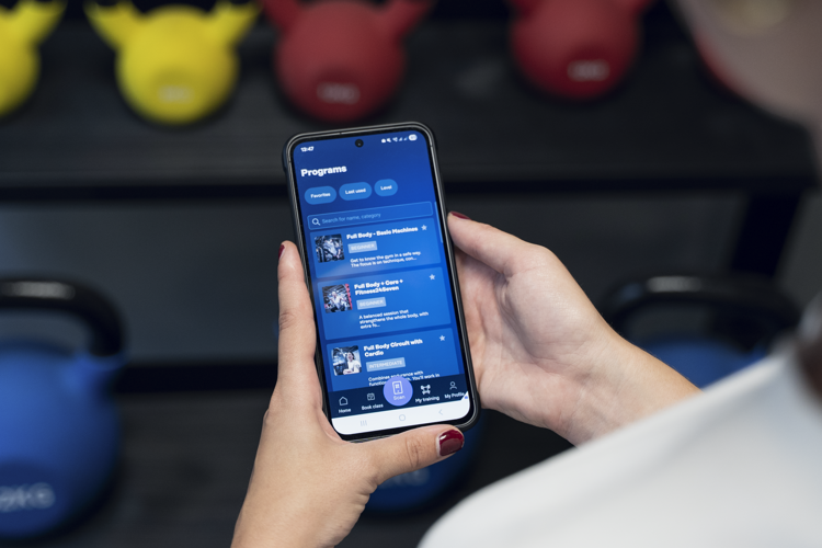 Medlem håller i mobil med Fitness24seven träningsprogram i appen